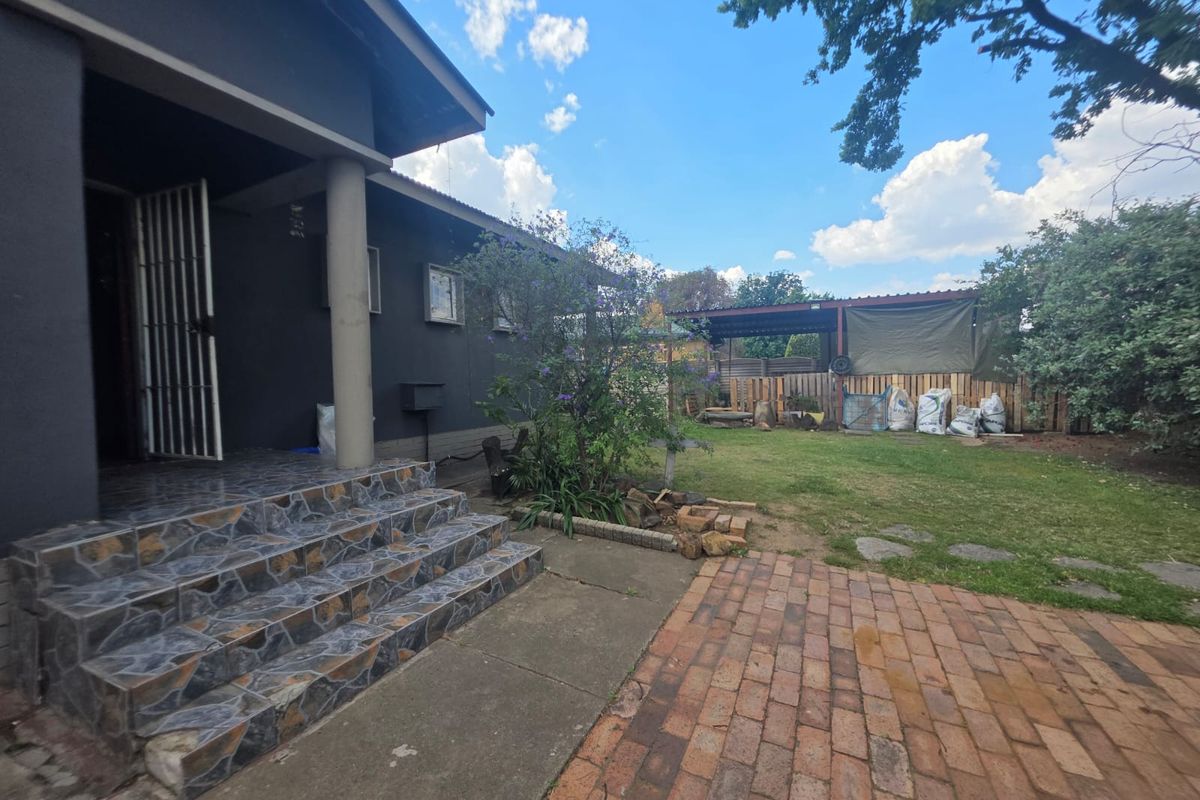 Rear exterior view featuring a tiled entrance, brick paved patio, lawn area, and a timber-fenced carport structure in the backyard.