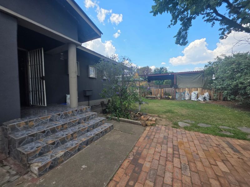 Rear exterior view featuring a tiled entrance, brick paved patio, lawn area, and a timber-fenced carport structure in the backyard.
