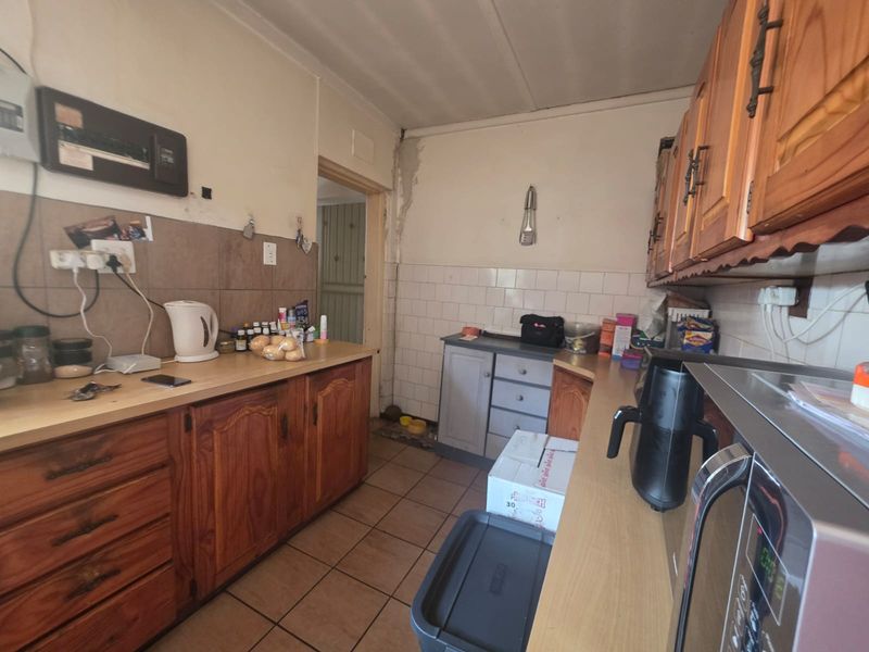 A functional kitchen featuring wooden cabinetry, tiled backsplash, and tiled flooring, currently showing signs of wear and requiring cosmetic updates.