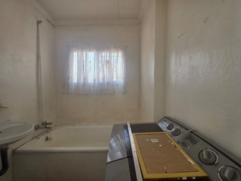 A dated bathroom featuring a built-in bathtub and wall-mounted basin, requiring cosmetic updates and wall refinishing to improve its overall condition.