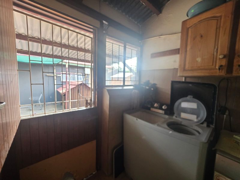 A functional laundry area featuring built-in wooden cabinetry, tiled splashbacks, and direct access to the exterior through a security gate.