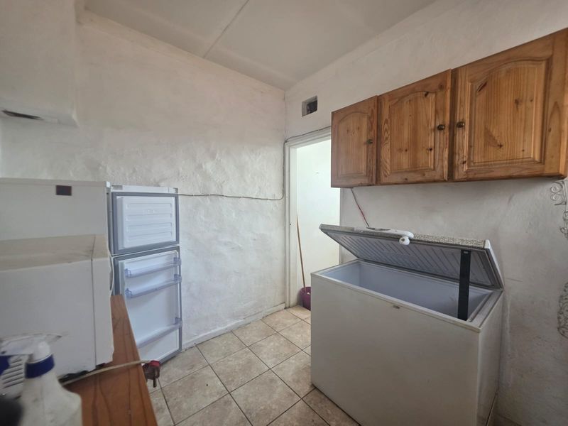 A functional scullery area featuring wall-mounted wooden cabinetry and tiled flooring, requiring cosmetic updates to the wall finishes and electrical presentation.