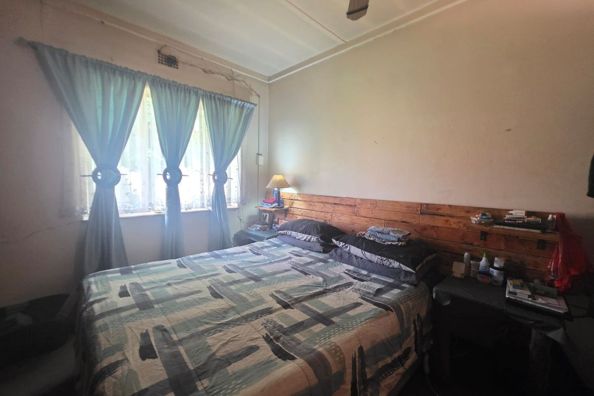 A bedroom featuring a ceiling fan and window with curtains, showing signs of wear on the walls requiring maintenance and cosmetic updates.