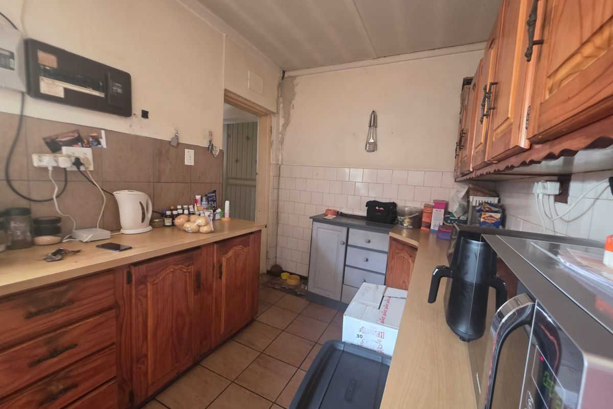 A dated kitchen featuring wooden cabinetry, tiled backsplash, and tiled flooring, requiring cosmetic updates to modernize the space.