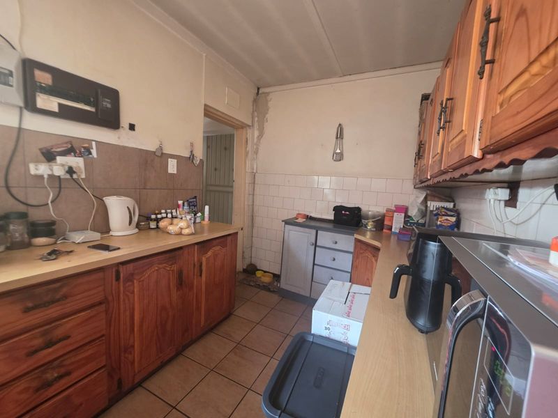 A dated kitchen featuring wooden cabinetry, tiled backsplash, and tiled flooring, requiring cosmetic updates to modernize the space.