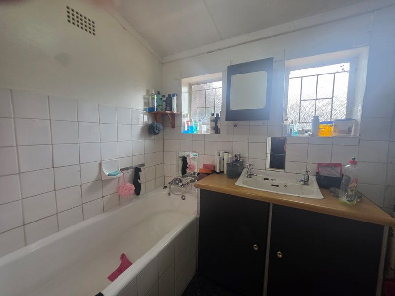 A functional bathroom featuring a bathtub, vanity cabinet with basin, and tiled walls. The space would benefit from modern updates to finishes.