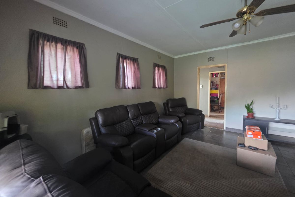 A living room featuring tiled flooring, a ceiling fan, and neutral wall finishes, providing a functional space with access to an adjacent room.