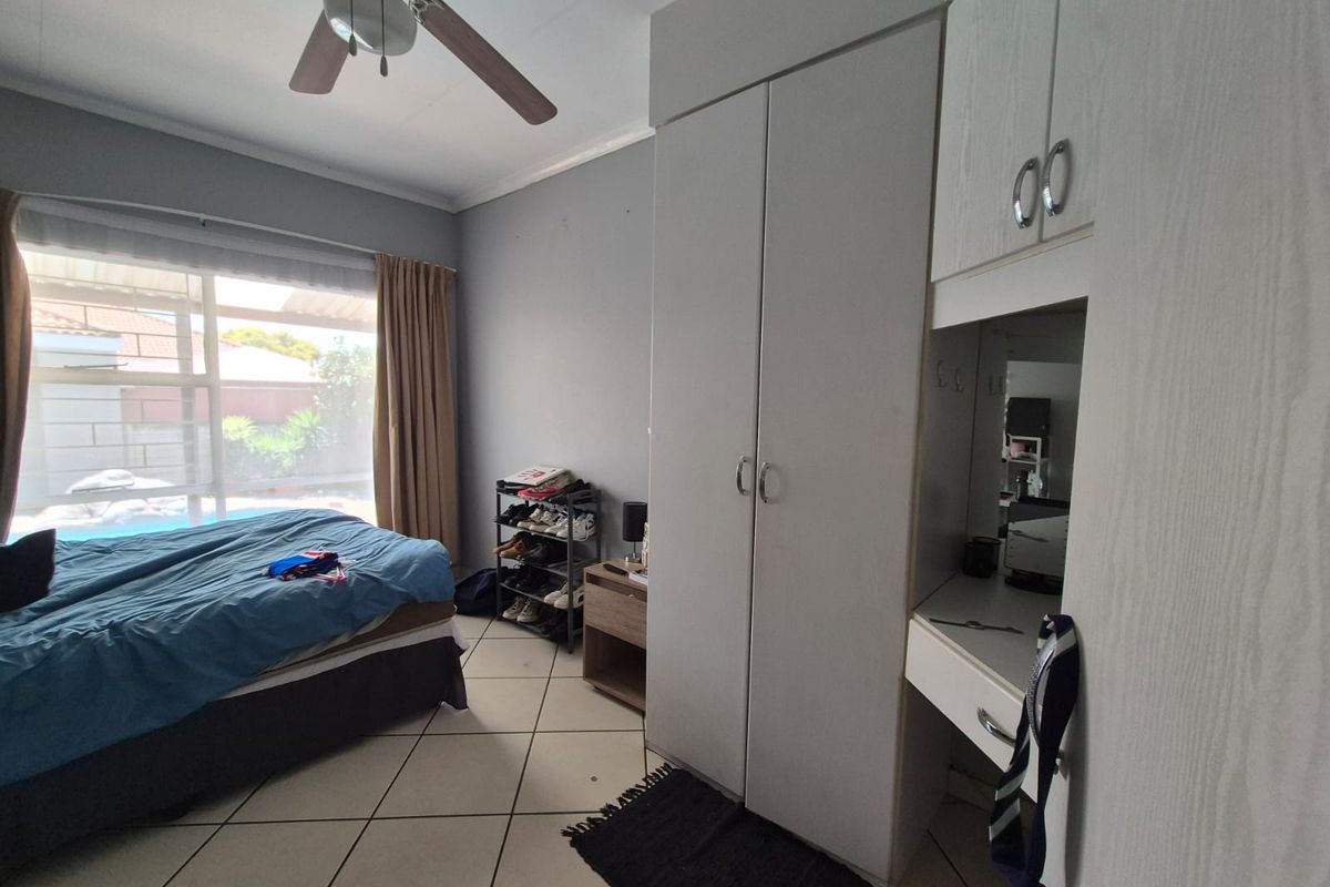 A functional bedroom featuring built-in cupboards, tiled flooring, and a ceiling fan, with large windows providing natural light.