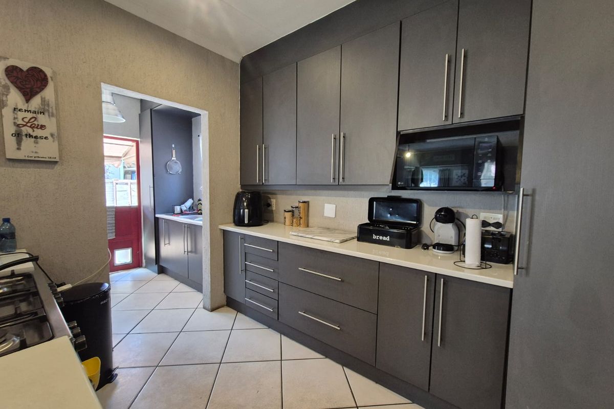 Modern kitchen featuring dark grey cabinetry, stone countertops, built-in microwave, and tiled flooring, with an adjacent scullery area visible through the doorway.