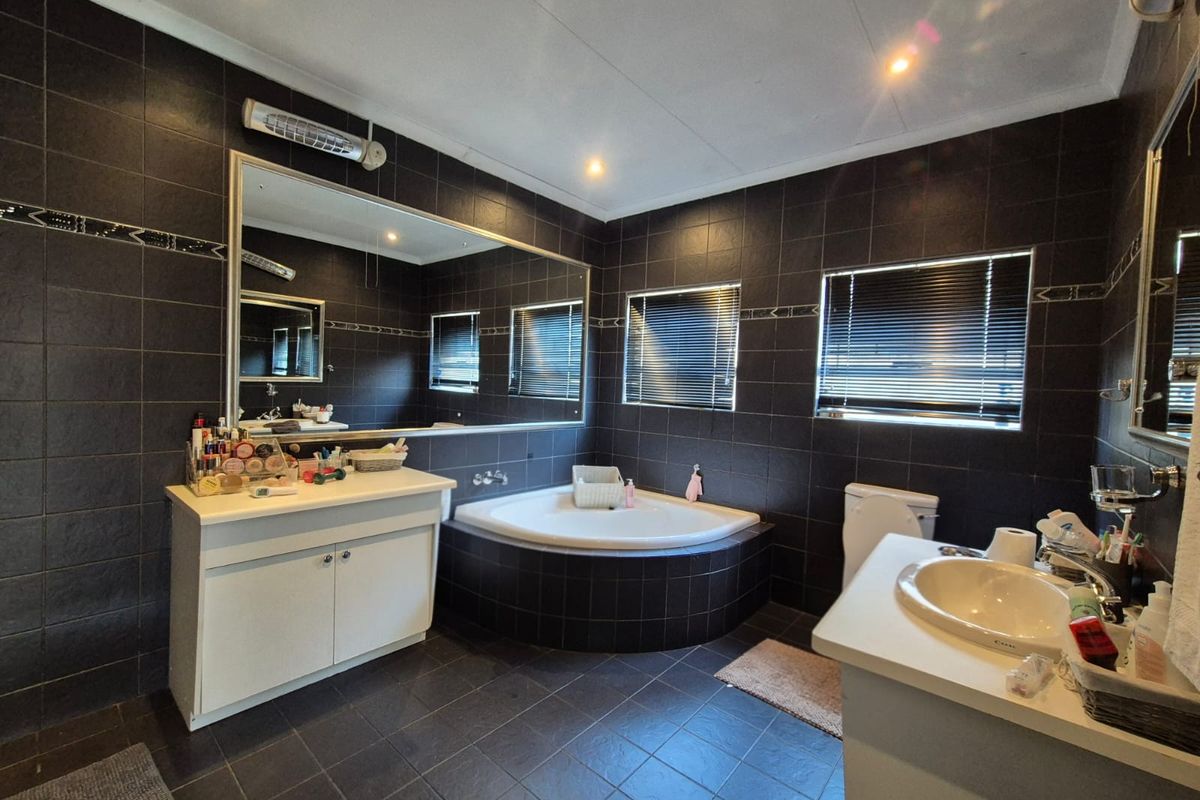 Spacious bathroom featuring dark tiled walls and floors, a corner bathtub, dual vanity units, and large mirrors with recessed lighting.