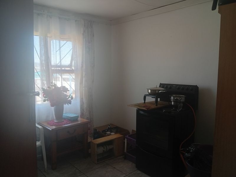 A compact kitchen area featuring tiled flooring, a window with security bars, and a freestanding stove.