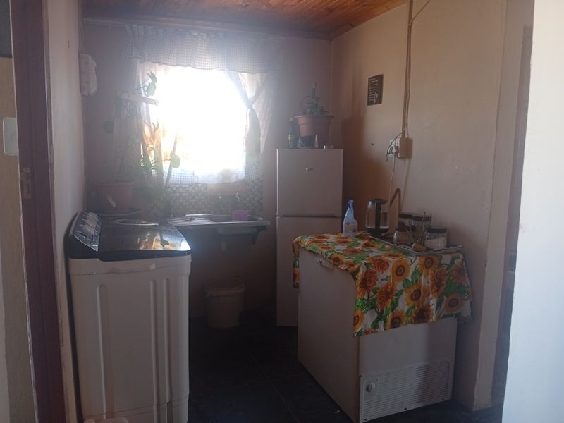 A functional laundry area featuring a stainless steel sink, tiled flooring, and a timber ceiling, requiring cosmetic updates to improve its overall condition.