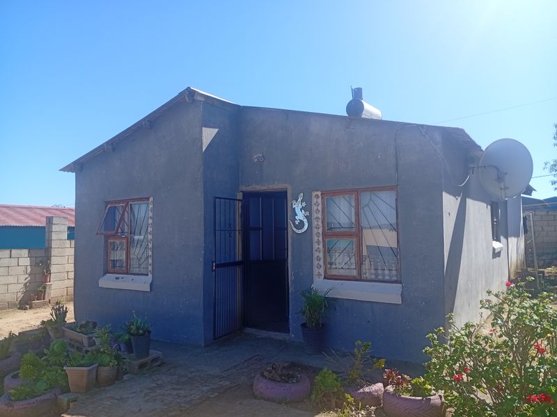 Front elevation of a single-story house featuring a corrugated metal roof, security gate, and installed solar water heating system.