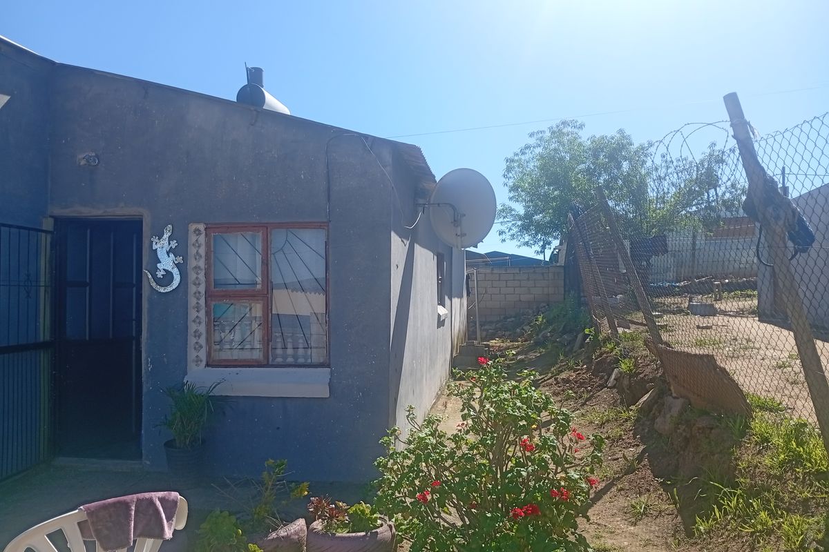 Rear exterior view of the property featuring a security gate, burglar bars, and perimeter chain link fencing.
