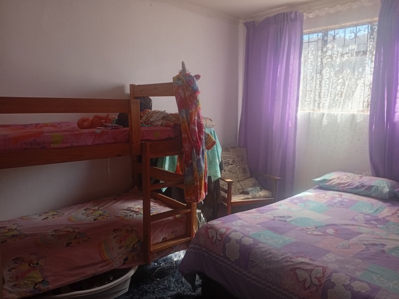A functional bedroom featuring a window with security bars, providing natural light and basic accommodation space.