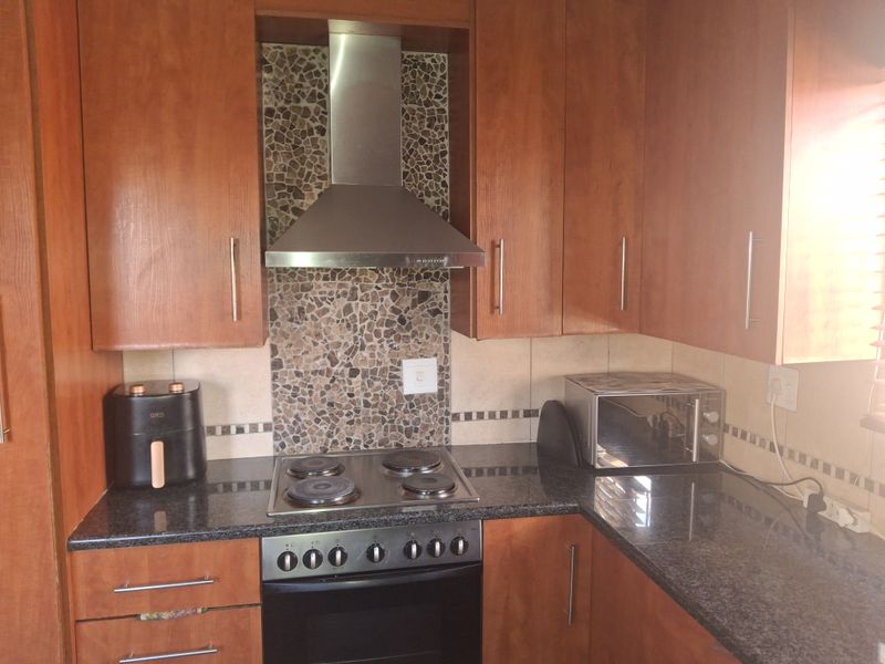 A functional kitchen featuring wood-finish cabinetry, granite countertops, a built-in electric oven and hob, and a decorative mosaic tile splashback.