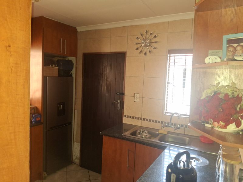 A functional kitchen featuring wooden cabinetry, granite countertops, a double sink, and tiled backsplash, requiring some cosmetic updates to the cabinetry and wall finishes.