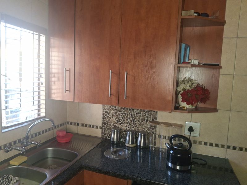 A functional kitchen area featuring wood-look cabinetry, granite countertops, a double stainless steel sink, and a decorative mosaic tile splashback.