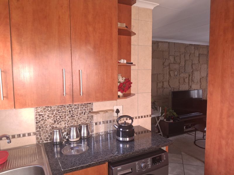 A functional kitchen featuring warm-toned wooden cabinetry, granite countertops, and a tiled backsplash, seamlessly flowing into an adjacent living area with a stone feature wall.