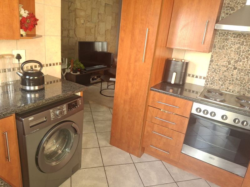A functional kitchen featuring granite countertops, built-in cabinetry, an integrated oven and hob, and tiled flooring, with an adjacent living area visible.