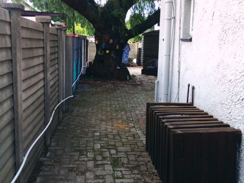 A side pathway featuring paved flooring, a precast concrete boundary wall, and a mature tree in the rear garden area.
