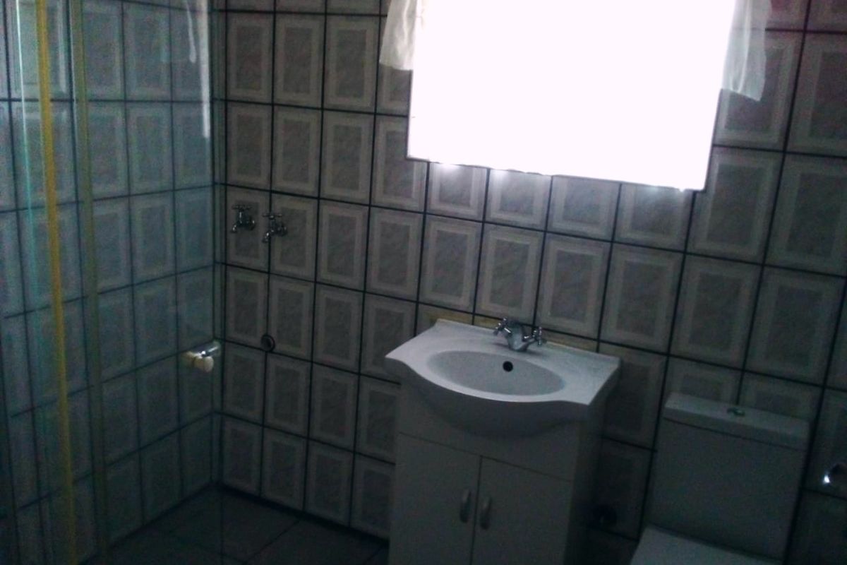 A functional bathroom featuring a shower enclosure, vanity basin, and toilet with full-height wall tiling.