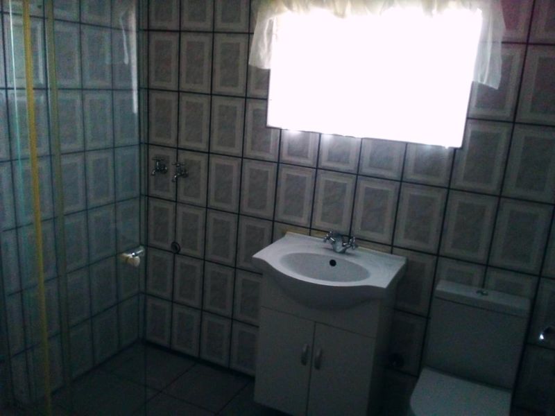 A functional bathroom featuring a shower enclosure, vanity basin, and toilet with full-height wall tiling.