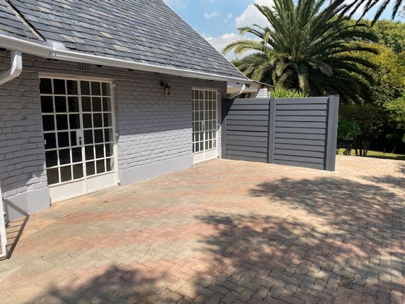 A well-maintained rear exterior view of the cottage featuring a slate roof, painted brick walls, paved patio area, and a modern privacy screen.