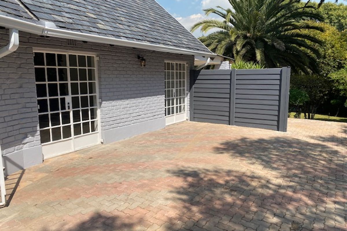 A well-maintained rear exterior view of the cottage featuring a slate roof, painted brick walls, paved patio area, and a modern privacy screen.
