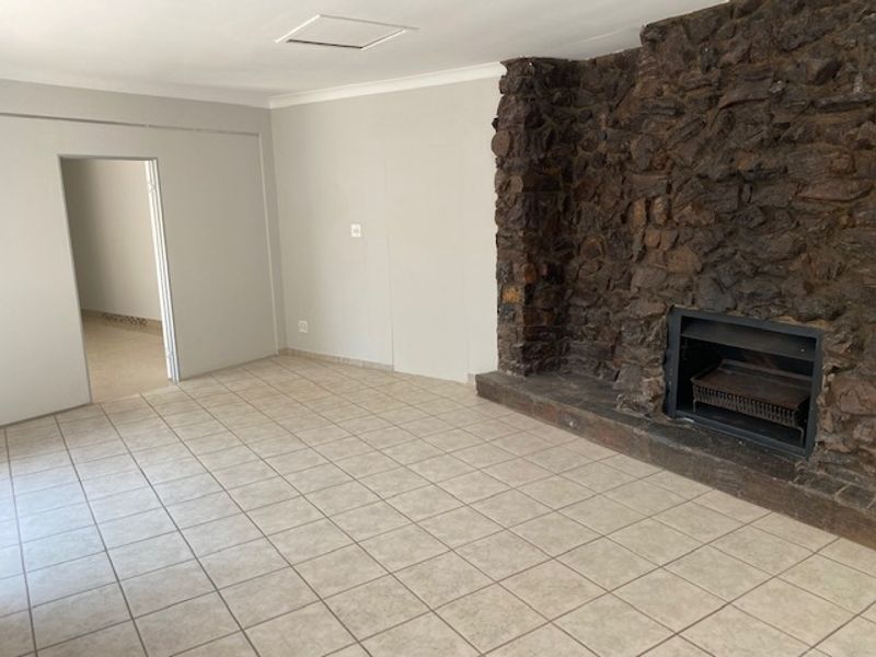 Spacious living room featuring a prominent stone fireplace, neutral tiled flooring, and clean wall finishes, offering a versatile blank canvas for interior design.