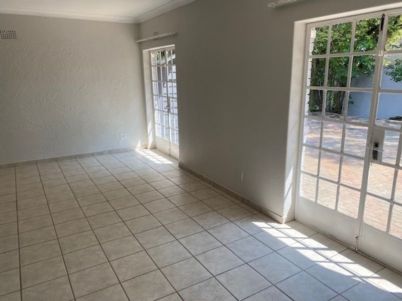 A bright, empty living room featuring neutral tiled flooring and double french doors providing direct access to the outdoor patio area.