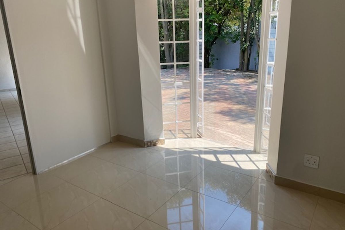A bright, empty living room featuring polished tiled flooring and white french doors that open directly onto a paved outdoor area.