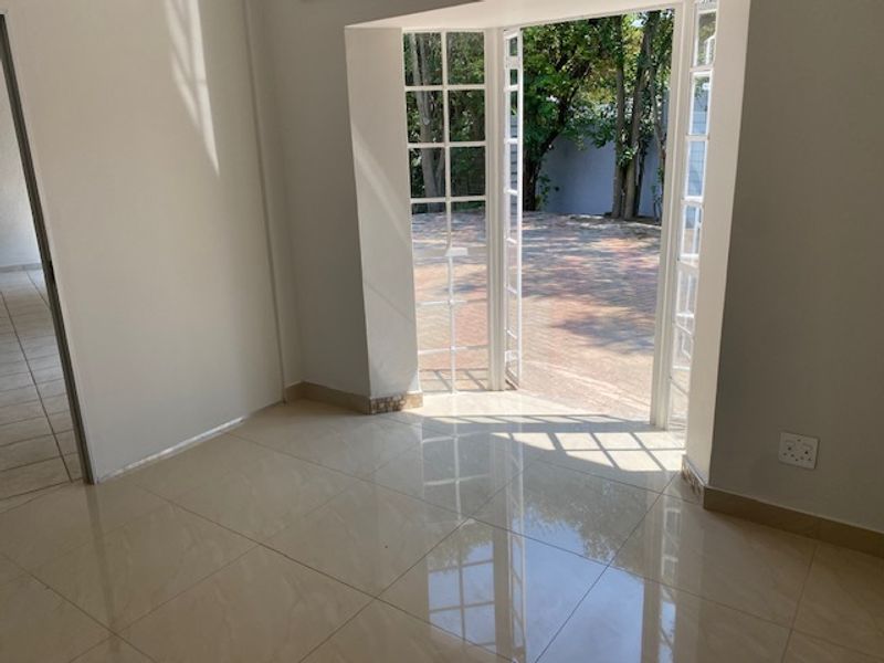 A bright, empty living room featuring polished tiled flooring and white french doors that open directly onto a paved outdoor area.