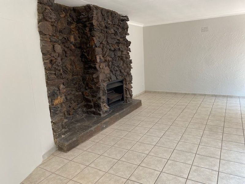 Spacious living room featuring a prominent rustic stone fireplace and neutral ceramic floor tiles, offering a clean, blank canvas for interior design.