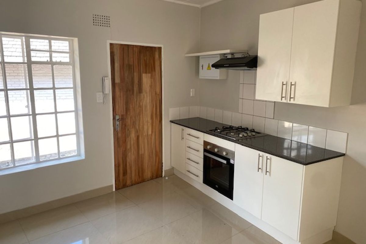 A clean, modern kitchen featuring white cabinetry, a gas hob, built-in oven, extractor fan, and tiled flooring in a bright, well-maintained space.