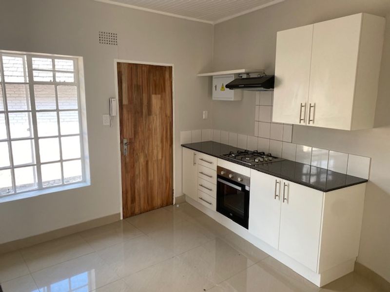 A clean, modern kitchen featuring white cabinetry, a gas hob, built-in oven, extractor fan, and tiled flooring in a bright, well-maintained space.
