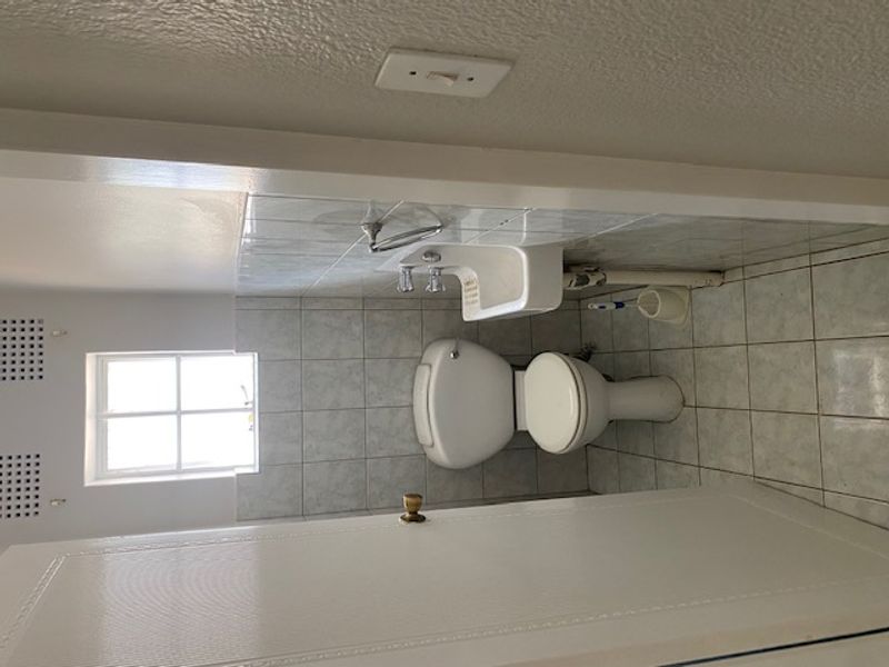 A compact, functional bathroom featuring a toilet, wall-mounted basin, and tiled finishes throughout, providing a clean and practical space.