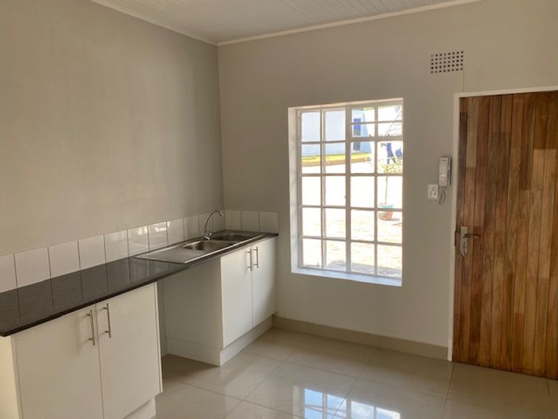 A clean, modern kitchen area featuring white cabinetry, granite countertops, a stainless steel sink, and tiled flooring, offering a bright and functional workspace.