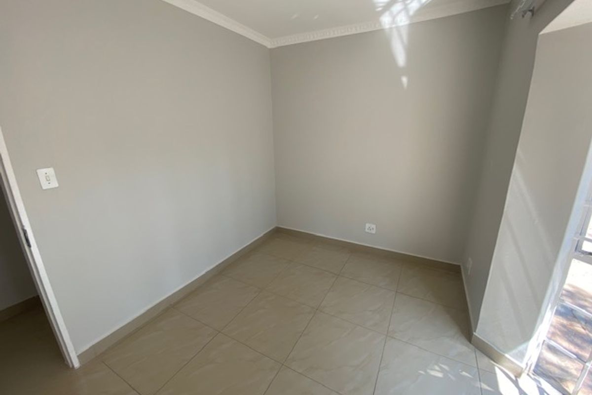 A bright, empty bedroom featuring neutral tiled flooring, clean walls, and decorative ceiling cornicing, offering a versatile space ready for personalization.