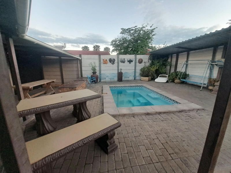 Outdoor entertainment area featuring a swimming pool, paved patio space, and covered sections enclosed by a perimeter wall.