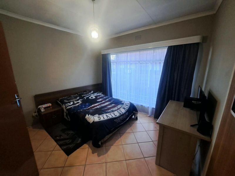 A functional bedroom featuring tiled flooring, a built-in headboard, and a large window with a curtain pelmet, offering a neutral base for personalization.