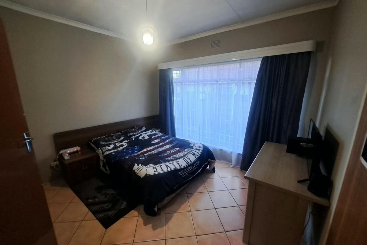 A functional bedroom featuring tiled flooring, a built-in headboard, and a large window with a curtain pelmet, offering a neutral base for personalization.