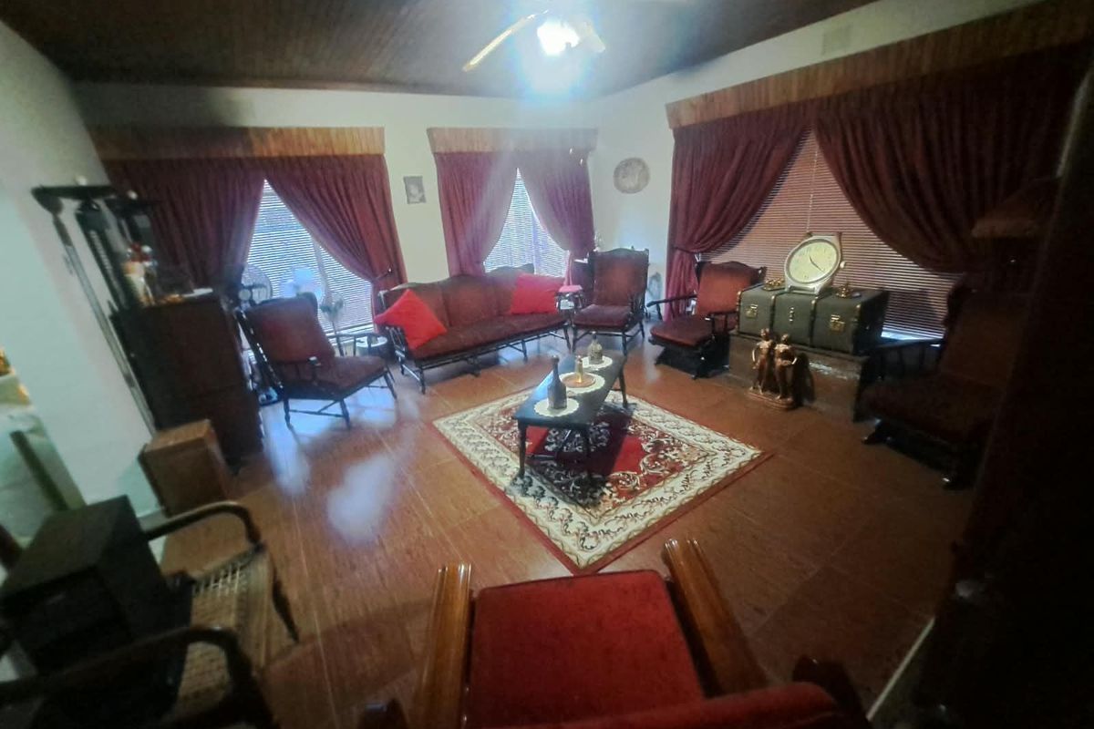 A traditional living room featuring a timber-paneled ceiling, ceiling fan, and tiled flooring, offering a classic layout with multiple windows.