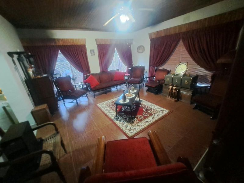 A traditional living room featuring a timber-paneled ceiling, ceiling fan, and tiled flooring, offering a classic layout with multiple windows.
