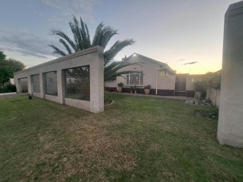 Front view of the property featuring a landscaped lawn, a prominent boundary wall, and secure access gate with security bars on the windows.