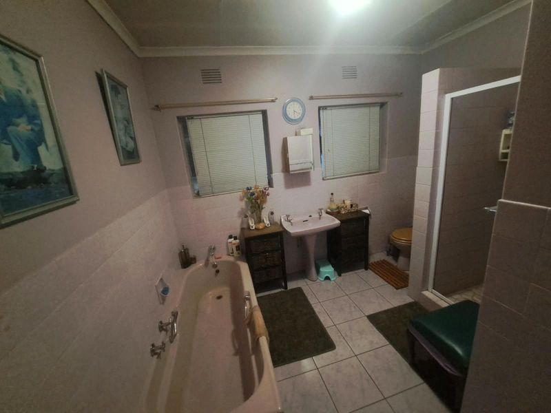 A functional bathroom featuring a pedestal basin, built-in bathtub, separate shower enclosure, and tiled finishes throughout.
