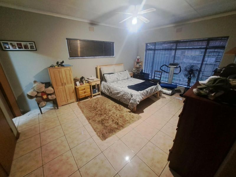 Spacious bedroom featuring tiled flooring, a ceiling fan, and large windows with venetian blinds, offering a functional and well-lit living space.