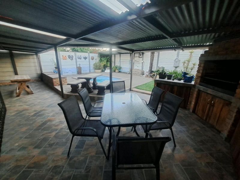 Covered outdoor entertainment area featuring a built-in brick braai, tiled flooring, and direct access to the swimming pool and garden space.