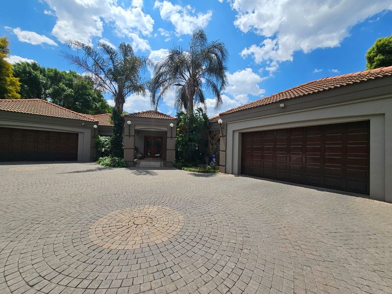 A well-maintained front exterior featuring a circular paved driveway, double garage doors, and a covered entrance with a tiled roof.