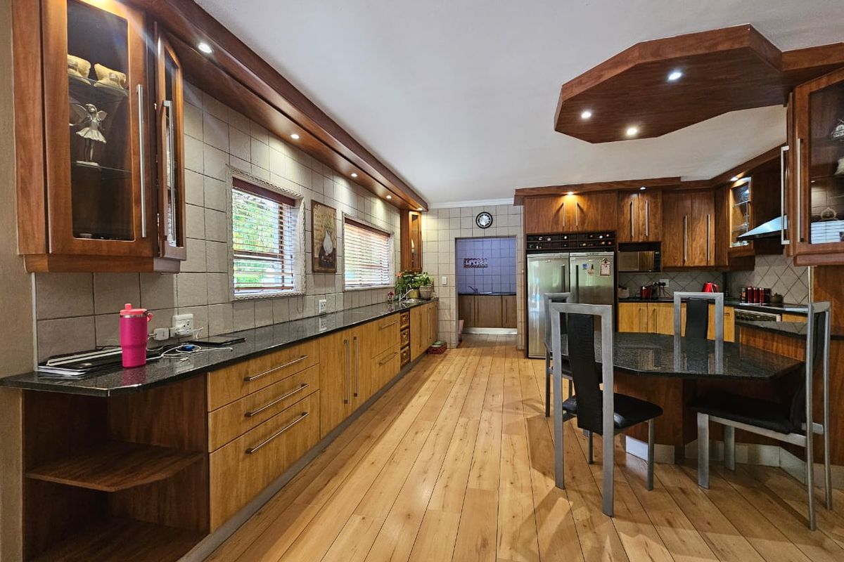Spacious kitchen featuring extensive wooden cabinetry, granite countertops, integrated appliances, and warm wooden flooring with a unique coffered ceiling design.